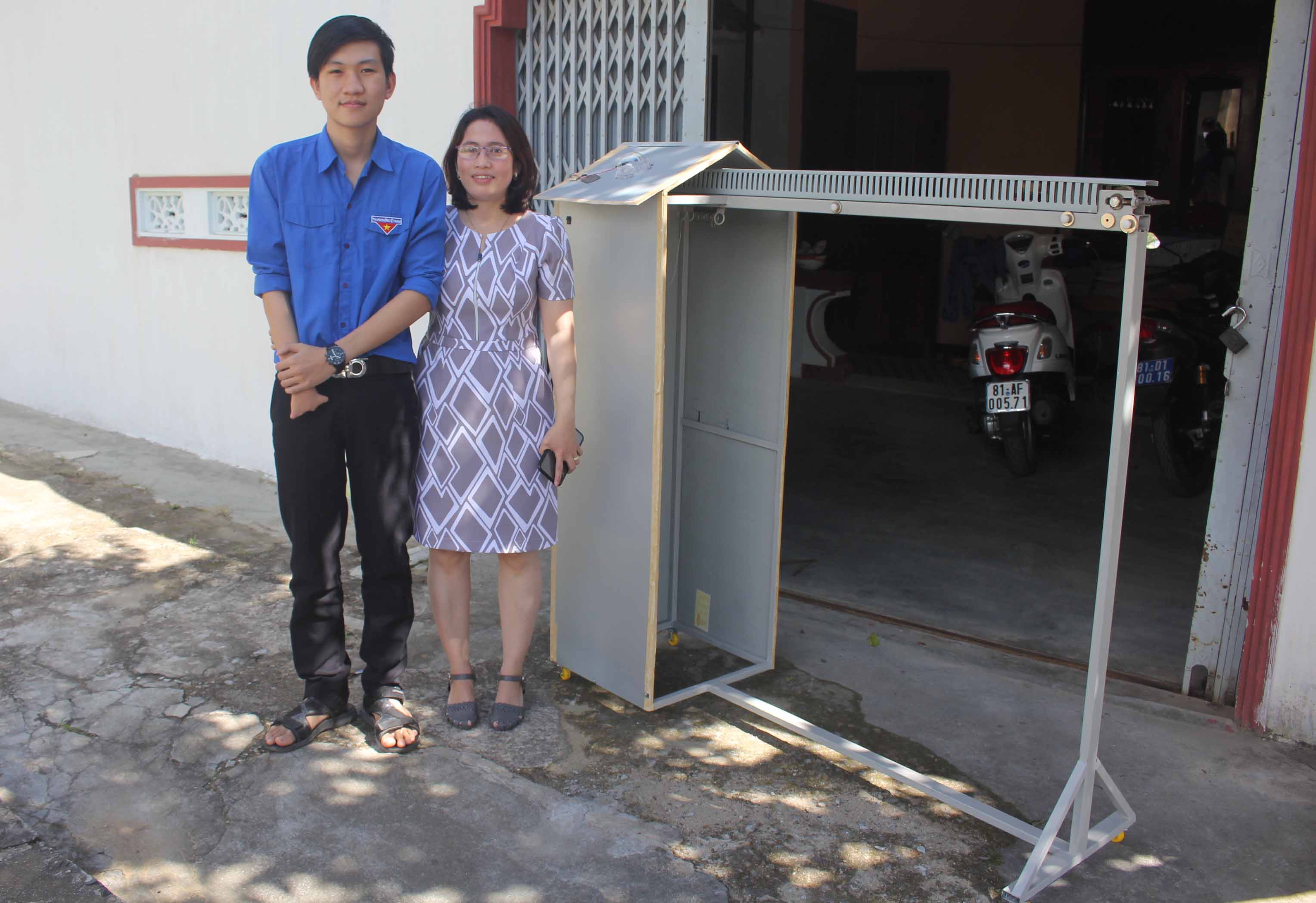  Em Trần Kế Tuấn Vương và cô giáo Tạ Thị Hạnh bên chiếc máy phơi đồ.  Ảnh: H.S