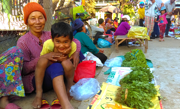 Bà Kpă H’Kut cùng đứa cháu bán rau vườn do bà trồng tại chợ Ia Mrơn. Ảnh: R.H