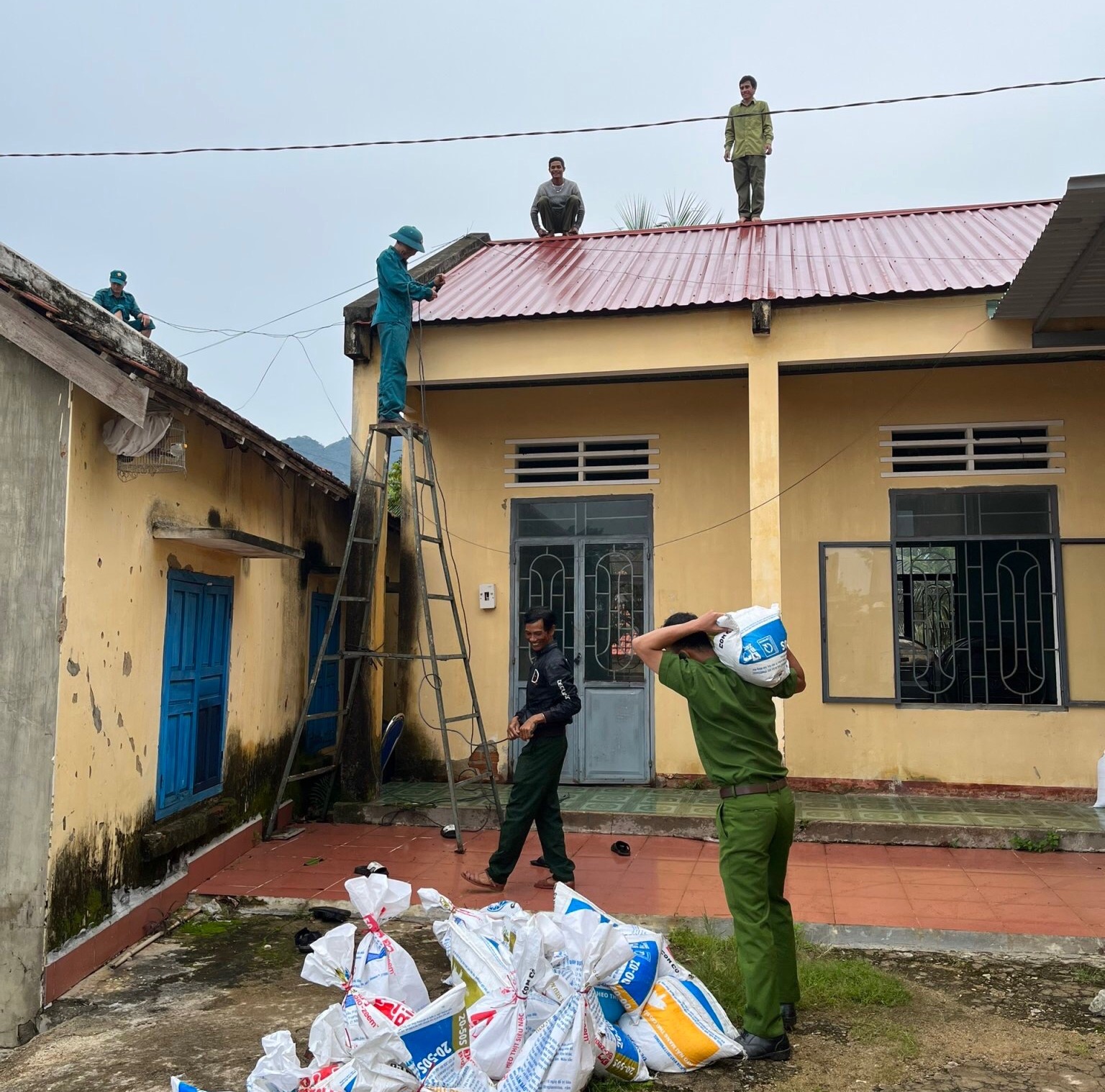 Lực lượng Công an, dân quân giúp người dân xã Lơ Ku, huyện Kbang chặn những bao cát trên mái nhà, hạn chế tốc mái. Ảnh:  An Phát