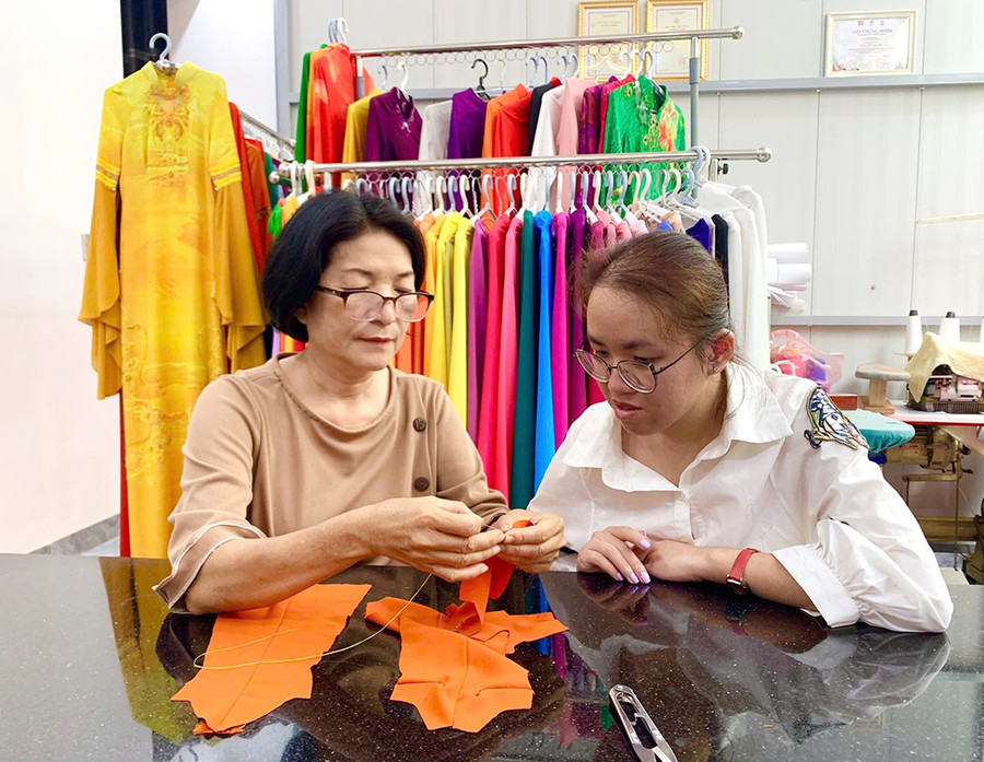 Nhà thiết kế Nguyễn Hạnh (bìa trái) hướng dẫn chị Trương Thị Thanh Huyền kỹ thuật may áo dài mini size. Ảnh: C.H Nhà thiết kế Nguyễn Hạnh (bìa trái) hướng dẫn chị Trương Thị Thanh Huyền kỹ thuật may áo dài mini size. Ảnh: C.H 1